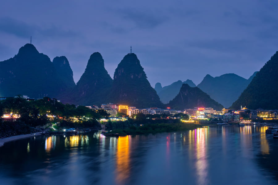 Vista nocturna de Yangshuo, China, con el río Li, las montañas kársticas iluminadas y los reflejos de la ciudad sobre el agua.