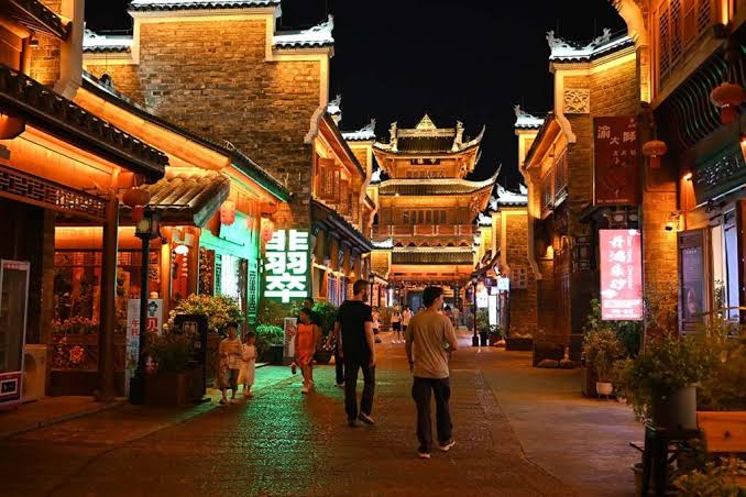 Calle tradicional china iluminada durante la noche, con edificios de arquitectura clásica, faroles y comercios que crean un ambiente vibrante para pasear y descubrir la cultura local.