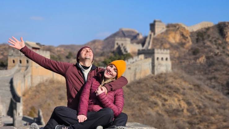 Pareja de viajeros disfrutando de una visita a la Gran Muralla China, rodeada de montañas y antiguas fortificaciones, durante un recorrido por uno de los monumentos históricos más emblemáticos del país.