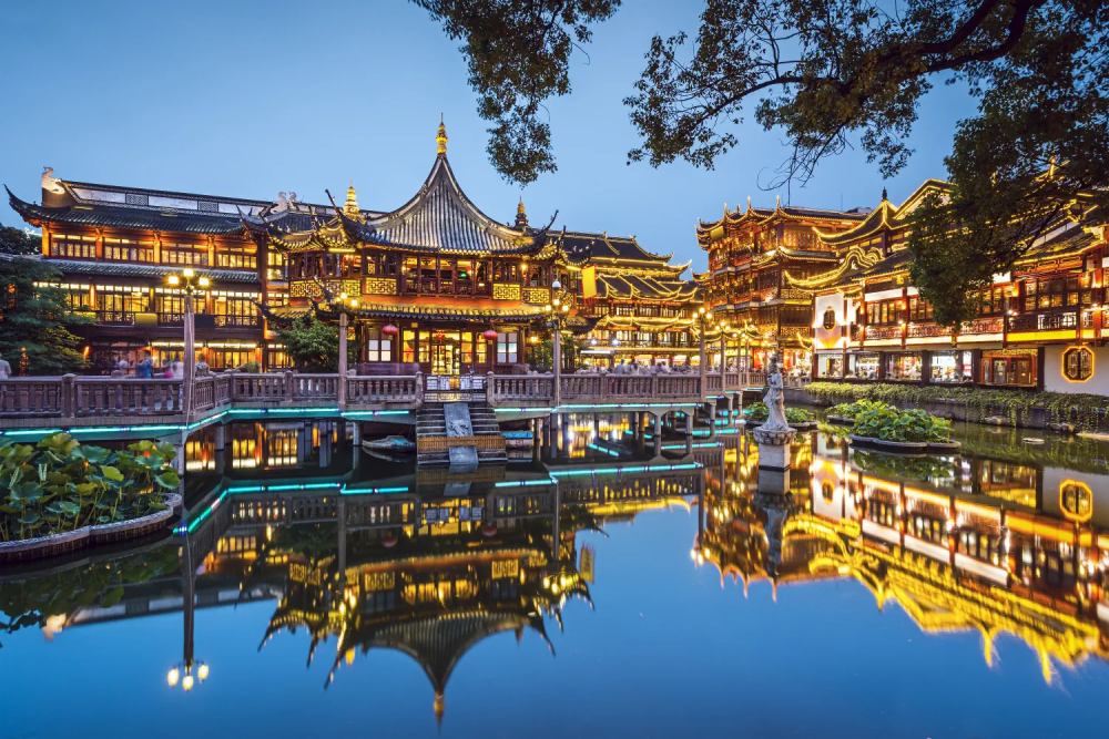 Jardín Yuyuan en Shanghái, uno de los lugares más emblemáticos para visitar en China, con arquitectura tradicional iluminada y un estanque que refleja sus edificios históricos.